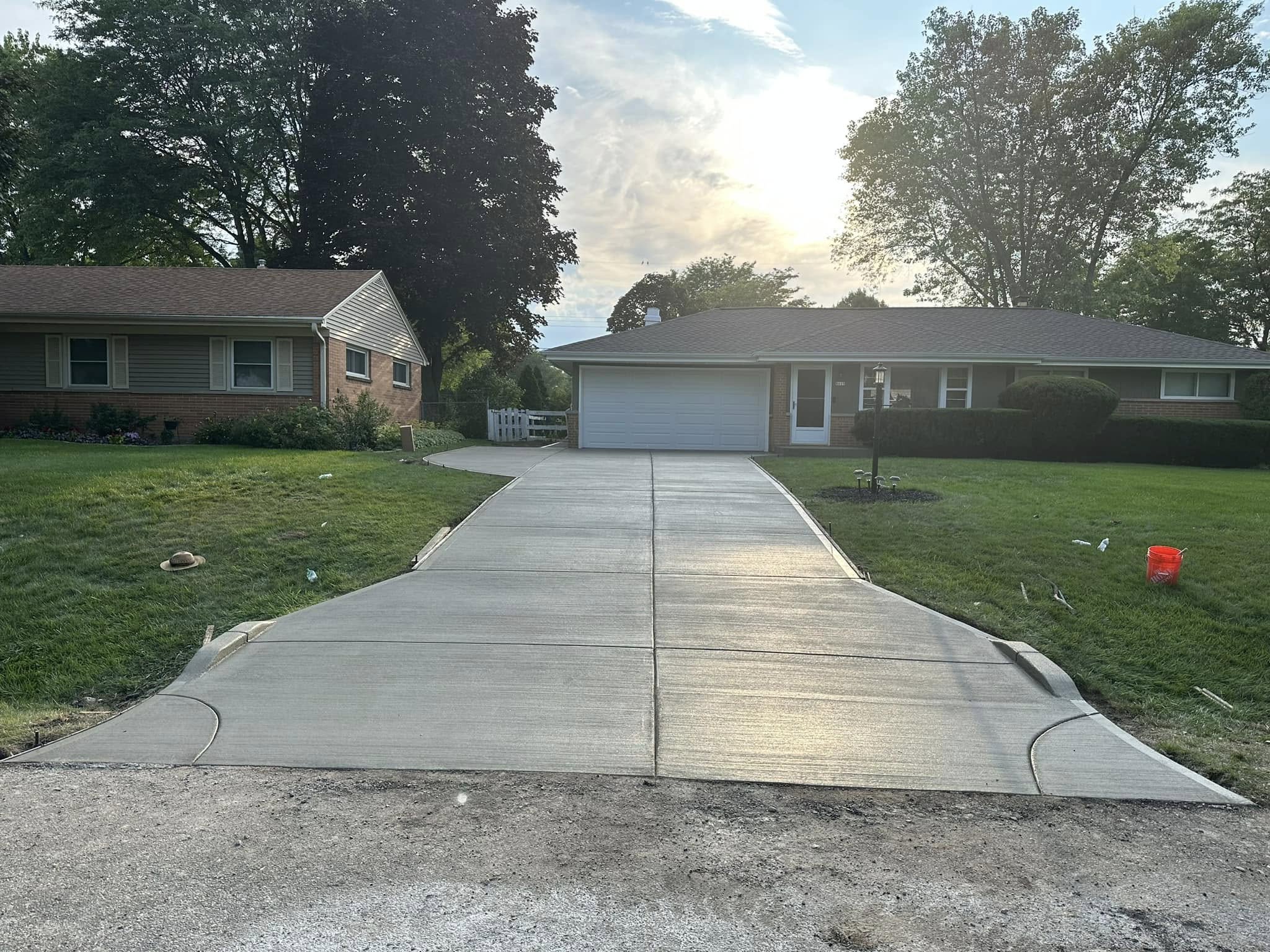 Freshly finished concrete driveway in front of brick ranch home with control joints photographed in evening light